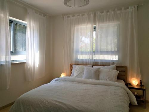 a bedroom with a large white bed with two windows at על שפת הבניאס in Sede Neẖemya