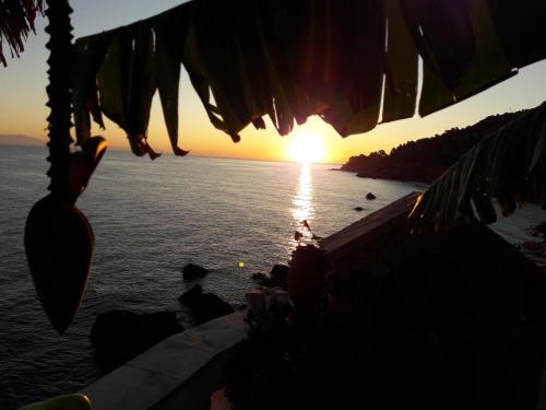 una puesta de sol sobre el agua con una persona sentada en una cornisa en Alkioni Studios en Karlovasi