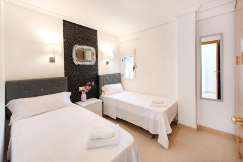 a white bedroom with two beds and a mirror at My Pretty Payma Apartamentos in Benidorm