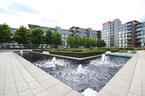 a fountain in a park with buildings in the background at iSTAY APARTMENTS at VIZION - Fully Equipped Modern Serviced Apartments with Balconies, Superfast Broadband, Free Allocated Parking Space, 24h Security, Rooftop Gardens, Located in Central MK in Milton Keynes