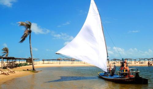 a boat with a white sail on the beach at Residence Kariri Beach Cumbuco in Cumbuco