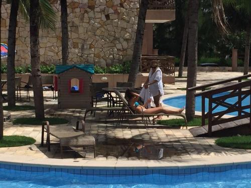 two people are sitting in chairs by a swimming pool at Residence Kariri Beach Cumbuco in Cumbuco