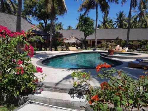 a swimming pool in a yard with palm trees and flowers at Trawangan Oasis in Gili Trawangan