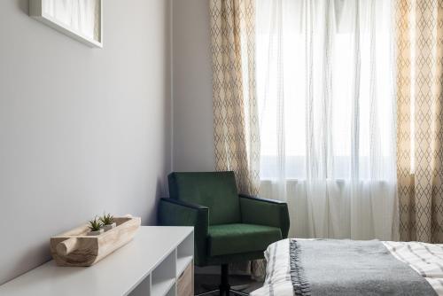a bedroom with a green chair next to a window at Csapô Apartment in Debrecen