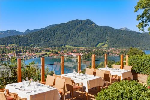 a restaurant with tables and chairs on a balcony with mountains at Hotel Leeberghof in Tegernsee