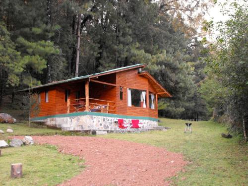 a log cabin with two red chairs in front of it at Cabañas Alpinas López Fontes in Valle de Bravo