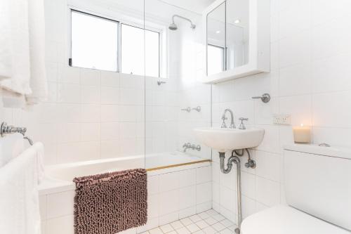 a white bathroom with a sink and a bath tub at Beachfront on Golden Mile in Sydney