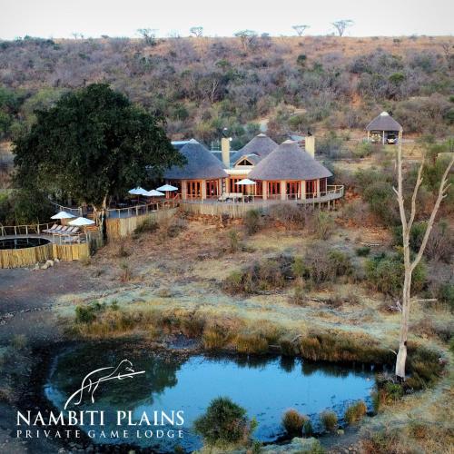 a house in the middle of a field with a pond at Nambiti Plains Lodge in Nambiti Private Game Reserve