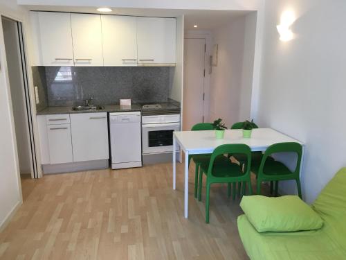 a kitchen with a white table and green chairs at Apartaments Muntaner I in Palamós