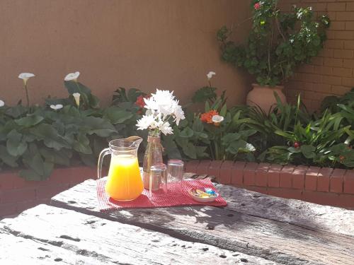 a table with a glass of orange juice and a vase of flowers at The Leopard Tree in Polokwane