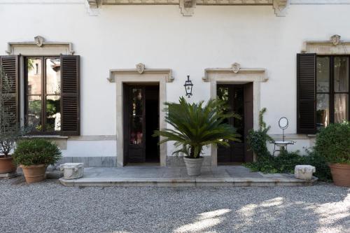 a white building with black shuttered windows and a plant at Hotel Locanda Dei Mai Intees in Azzate