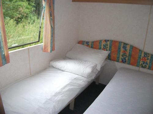 2 camas en una habitación pequeña con ventana en caravan nestled away amongst trees on edge of farm yard en Bala