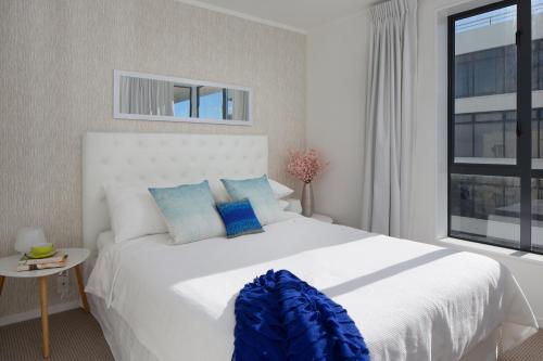 a bedroom with a large white bed with blue pillows at Ocean View Beach Escape - Top Floor Apartment, Mt Maunganui Base in Mount Maunganui