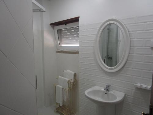 La salle de bains blanche est pourvue d'un lavabo et d'un miroir. dans l'établissement Pensão Residencial Luanda, à Tomar