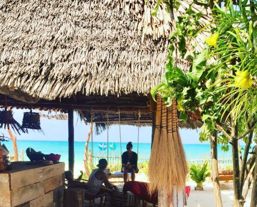 two people sitting under a straw hut on the beach at Zanzistar Lodge in Jambiani