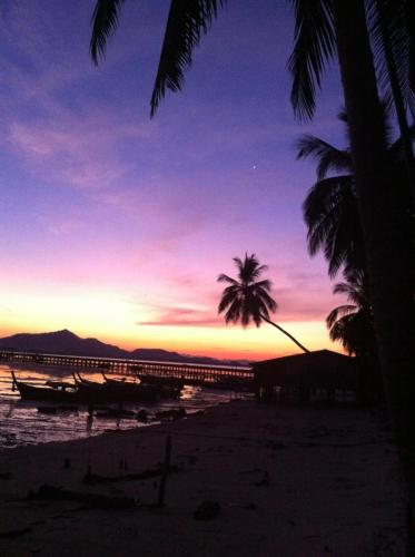 a sunset on a beach with a palm tree and a pier at Seaside home in Koh Mook