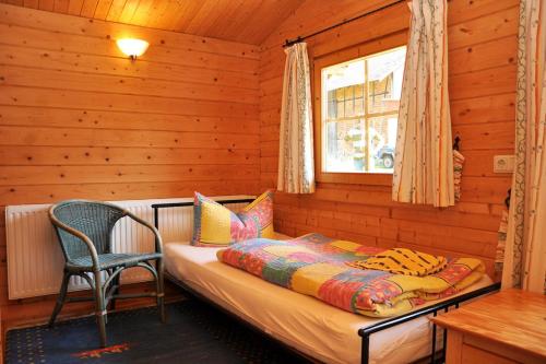 a bed in a wooden room with a chair and a window at Pension "AM RENNSTEIG" in Eisenach