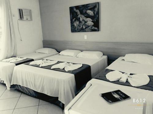 three beds in a hotel room with white sheets at Pousada Hippocampus in Juquei