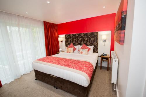 a bedroom with a large bed with red walls at Stanwell Hotel By Mercure in Stanwell