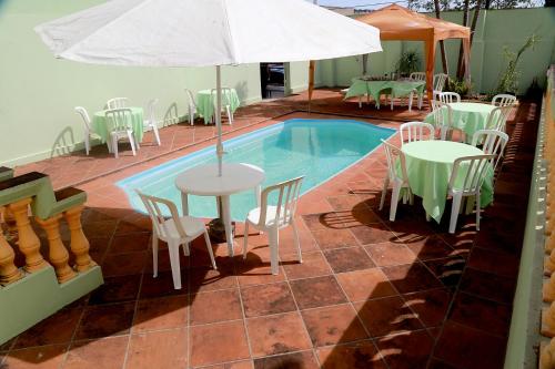 a pool with tables and chairs and an umbrella at Pousada Victor in Ribeirão Claro