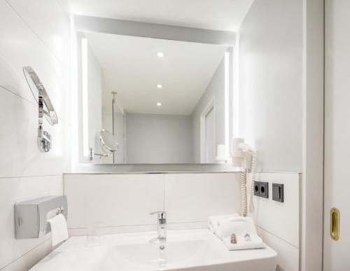 a white bathroom with a sink and a mirror at Ramada by Wyndham Flensburg City in Flensburg