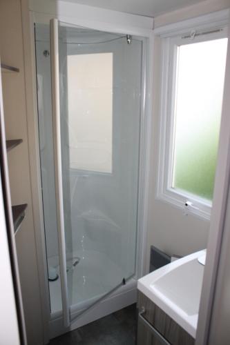 La salle de bains est pourvue d'une douche en verre et d'une fenêtre. dans l'établissement Camping des Roses, à Quend