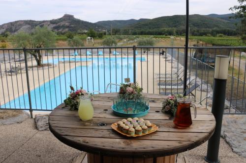 a wooden table with food and drinks on a balcony with a pool at Rev'ôthijol Vacances in Saint Alban Auriolles