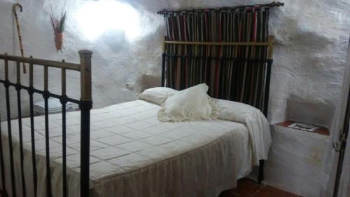 ein Schlafzimmer mit einem Bett mit weißer Bettwäsche und einem Regal in der Unterkunft Cueva Rural La Noguera in Pegalajar