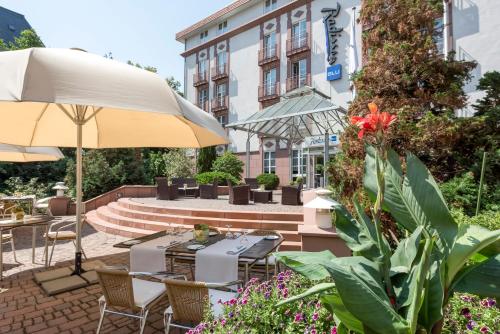 a patio with tables and chairs and an umbrella at Radisson Blu Hotel Halle-Merseburg in Merseburg