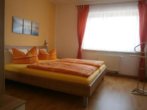 ein Schlafzimmer mit einem Bett mit orangefarbenen Kissen und einem Fenster in der Unterkunft Ferienwohnung Fischer in Jena