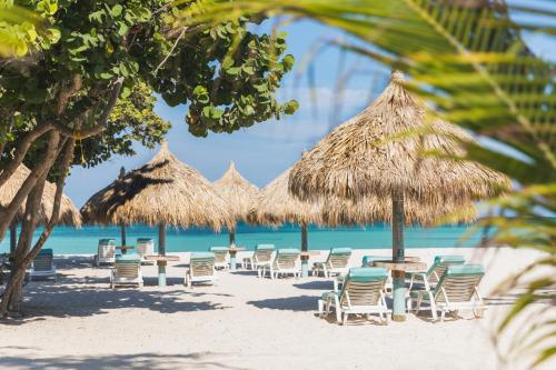 a beach with chairs and tables and straw umbrellas at Boardwalk Boutique Hotel Aruba - Adults Only in Palm-Eagle Beach