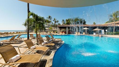 a large swimming pool with chairs and the ocean at Pierre Mundo Imperial Riviera Diamante Acapulco in Acapulco