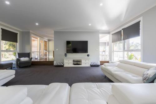 a living room with white furniture and a flat screen tv at QUPI HOUSE formerly Rex's Yarra Valley House in Healesville