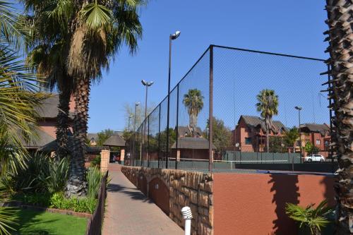 a tennis court with a fence and palm trees at Alendo Apartments in Johannesburg