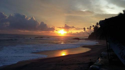 a sunset on a beach with the ocean at Seasons Four Eco Friendly Treehouse in Matara