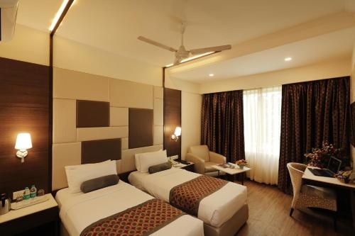 a hotel room with two beds and a desk at Hotel Pai Vista in Mysore