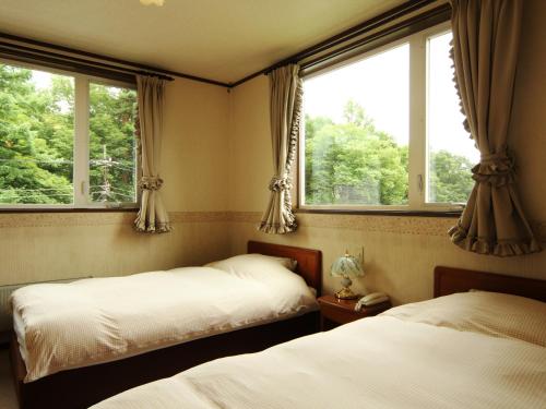 two beds in a room with two windows at Pension Raisin in Kusatsu