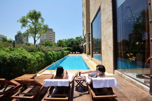 two women sitting in chairs next to a swimming pool at Reston Hotel in Jounieh