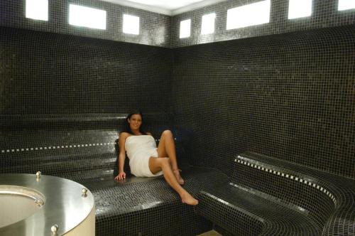 une femme assise sur un banc dans une salle de bains carrelée de noir dans l'établissement Appartamento Gemelli, à Cavalese