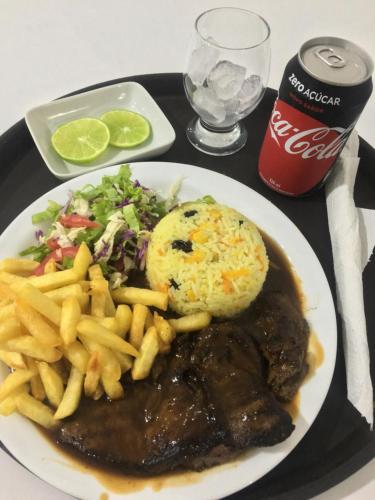 a plate of food with meat and french fries and a soda at Entre Rios Hotel in Picos