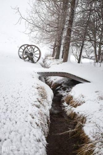 a snow covered bridge in a park with a creek at Vallakot Farm Guesthouse in Laugar