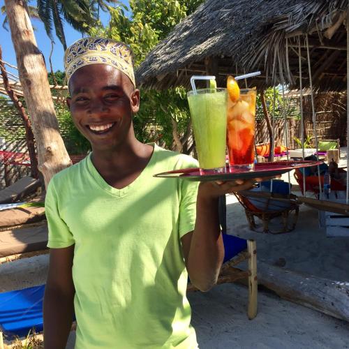 a man holding a tray with two drinks on it at Zanzistar Lodge in Jambiani