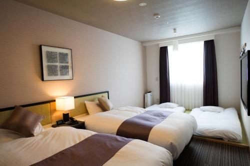a hotel room with three beds and a window at Hotel La'gent Plaza Hakodate Hokuto in Hokuto
