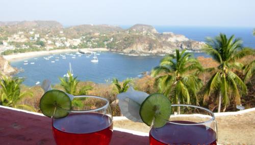 two glasses of wine sitting on a ledge with a beach at Angel del Mar in Puerto Ángel