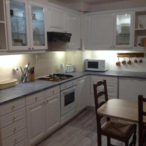 une cuisine avec des armoires blanches, une table et une cuisinière dans l'établissement Chez Michel, à Le Bonhomme