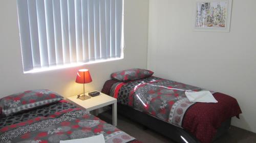 a bedroom with two beds and a table with a lamp at Parkside Apartments Parramatta in Sydney