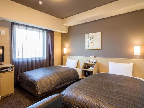 a hotel room with two beds and a television at Hotel Route Inn Minami Yokkaichi in Yokkaichi