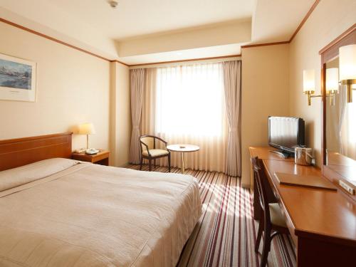 a hotel room with a bed and a desk and a television at Hotel Crown Palais Kokura in Kitakyushu