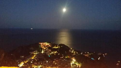 a full moon rising over an island in the ocean at Sciala' in Taormina