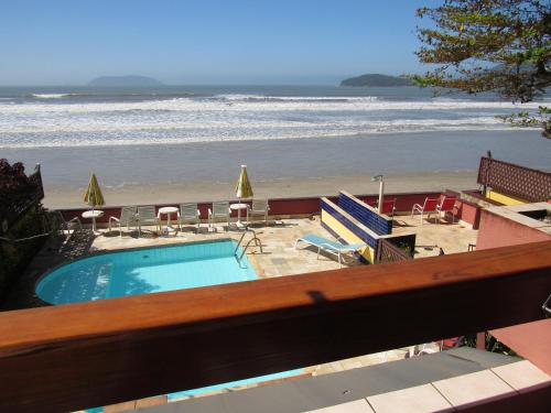 a swimming pool and the beach with chairs and umbrellas at Pousada Casa na Praia in Ubatuba